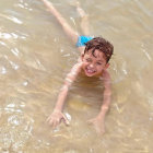 Child wading in clear sunlit water with gentle ripple and sandy bottom.