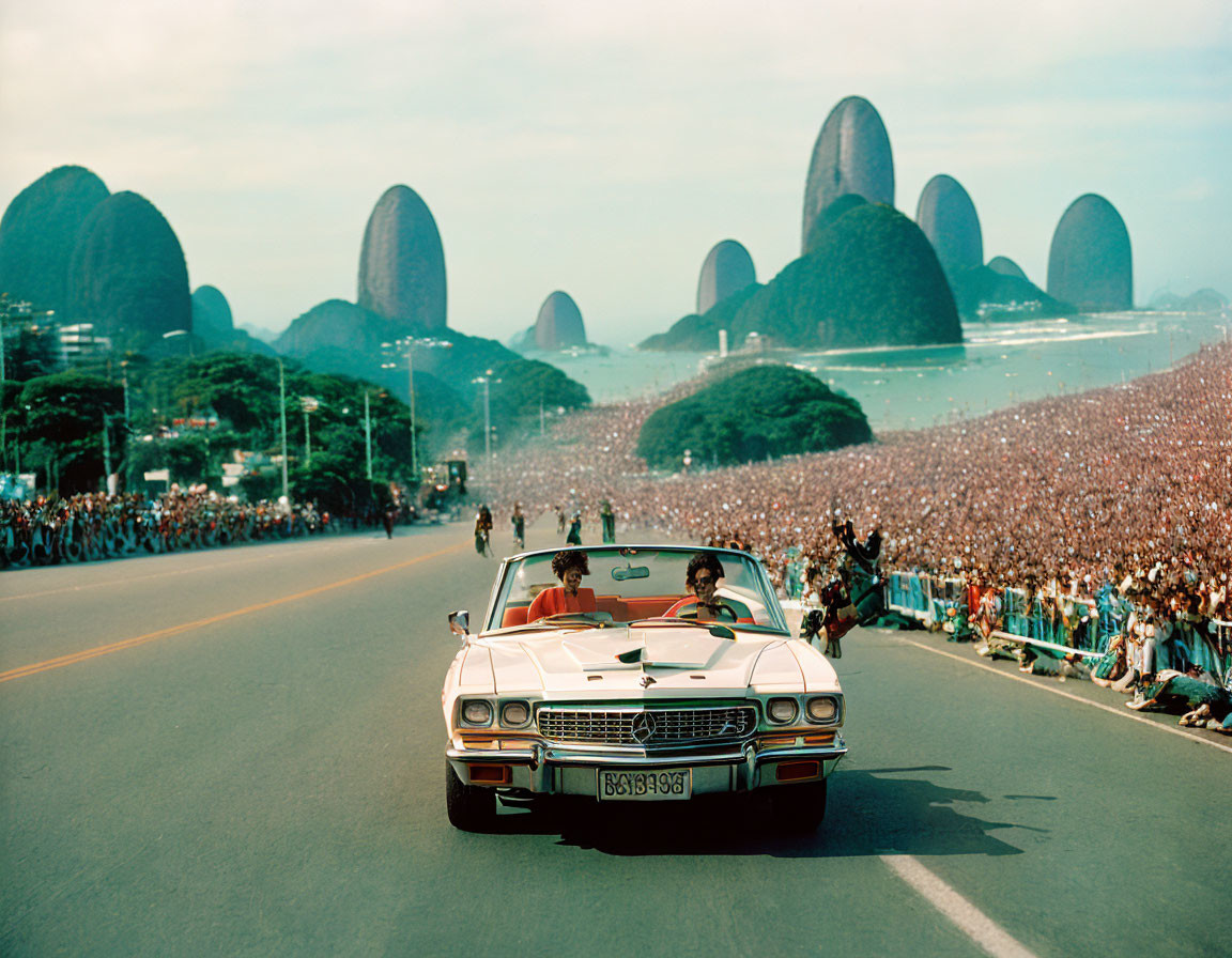 Vintage convertible car with passengers on coastal road, surrounded by crowds and mountain peaks