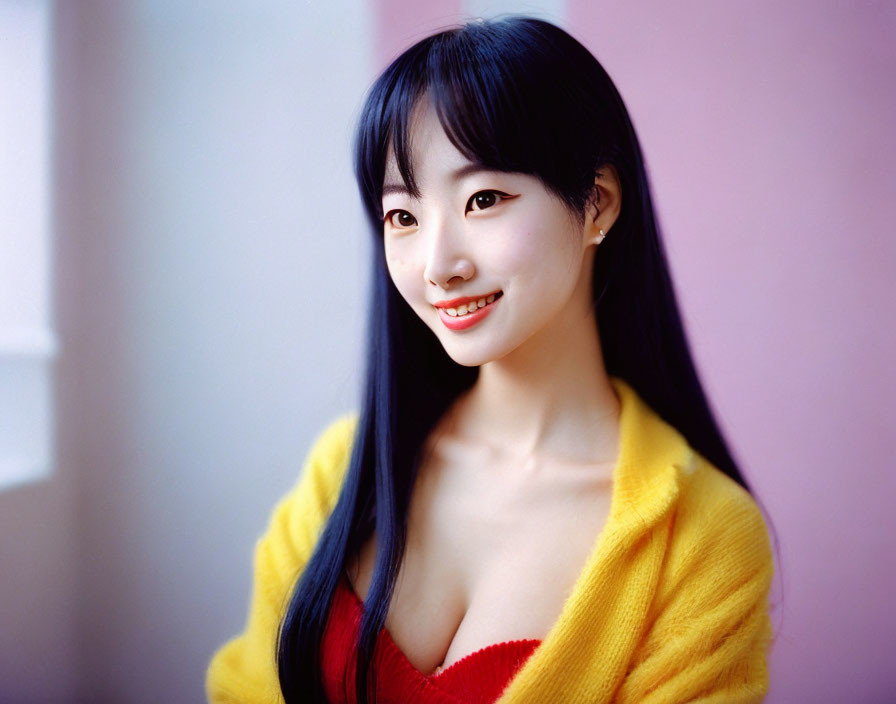 Smiling young woman with black hair in yellow cardigan on pink backdrop
