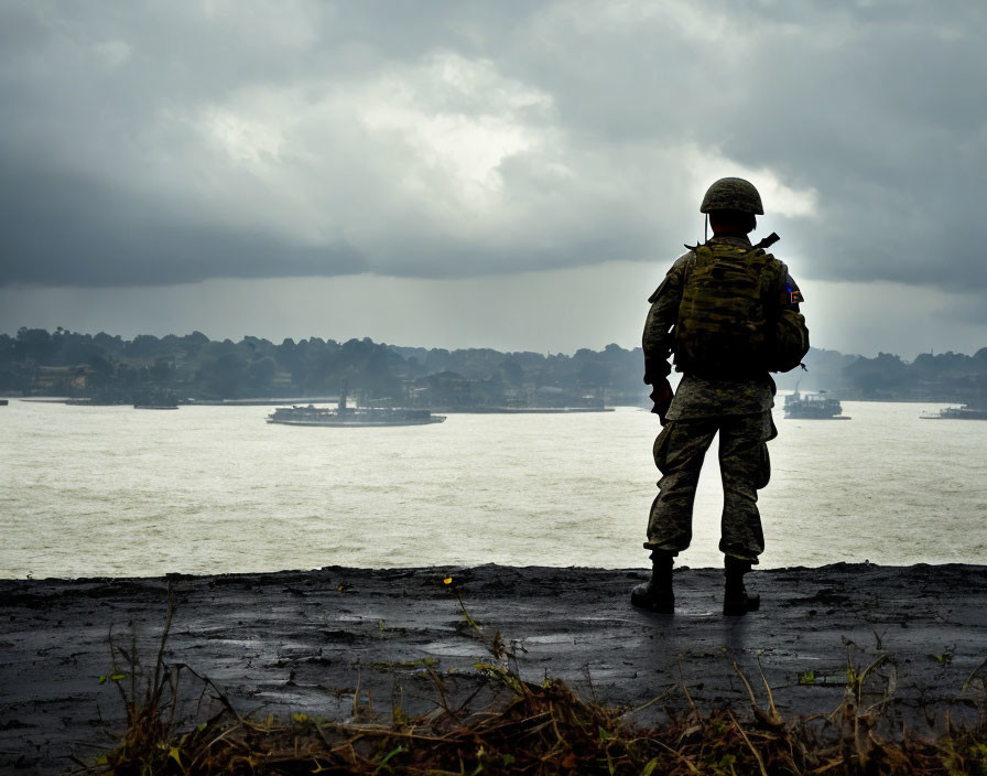 Camouflaged soldier gazes at shoreline waterscape