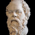 Realistic sculpture of man's head with full beard, mustache, and wavy hair on black