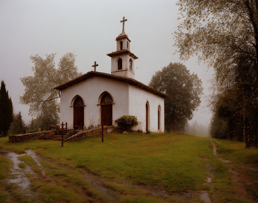 White chapel with bell tower in misty landscape and muddy path