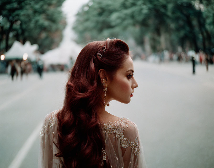 Red-haired woman in embroidered dress gazes thoughtfully in street scene.