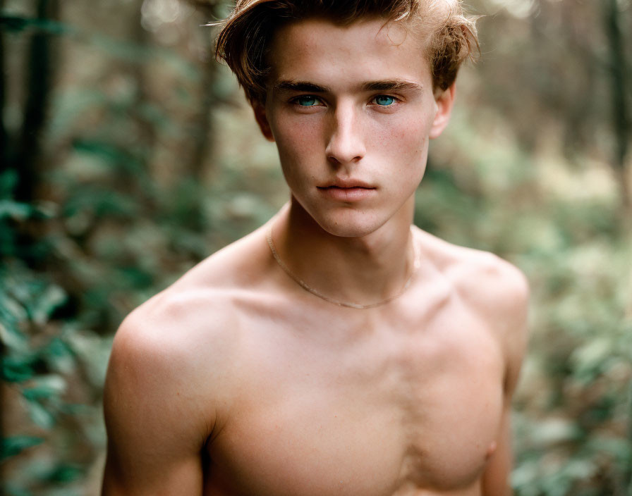 Blue-eyed shirtless man with necklace in forest setting