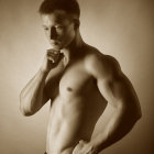 Muscular man in contemplative pose, sepia-toned monochrome photo.