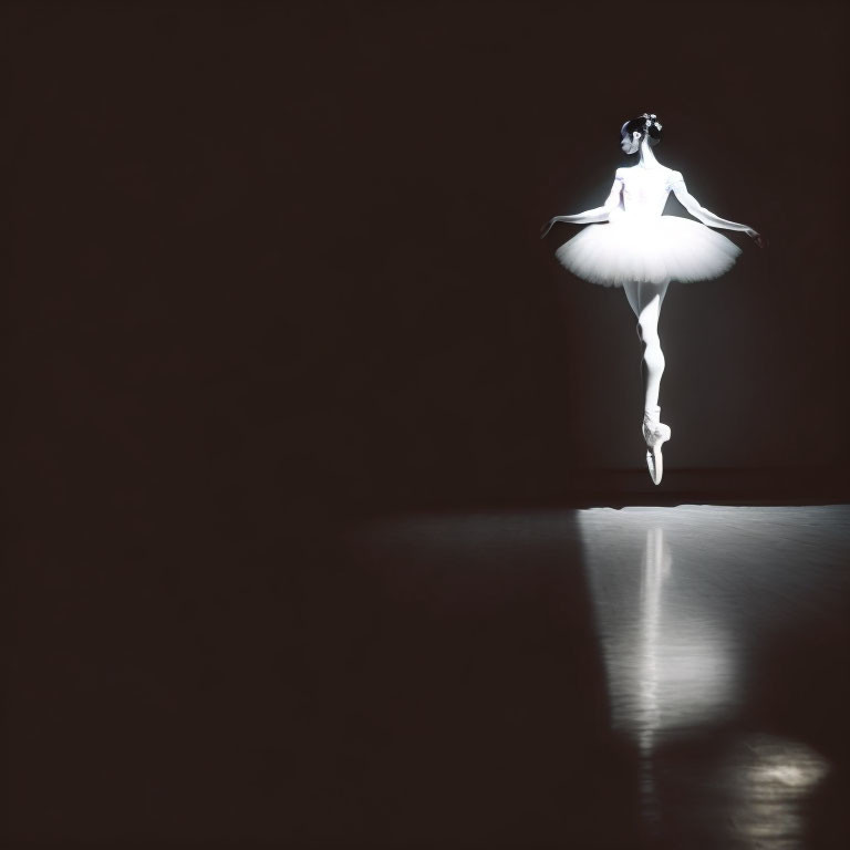 White tutu ballerina in dance pose on tiptoe with beam of light on dark background