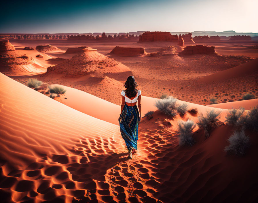 Person standing in desert dunes under blue sky with warm sunlight.