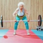 Elderly woman with white hair lifting barbell in gym