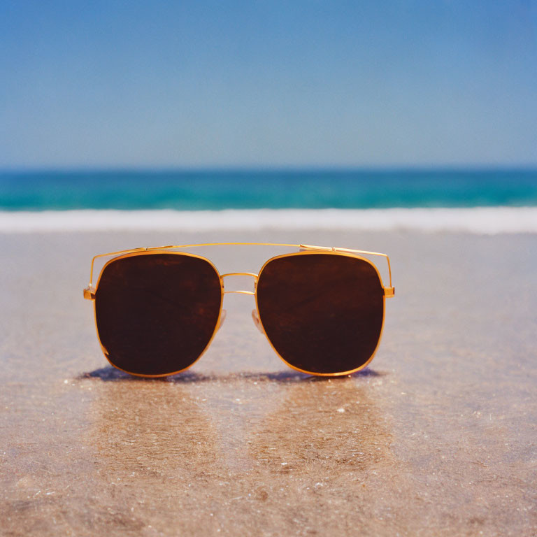 Sunglasses on sandy beach with ocean and blue sky
