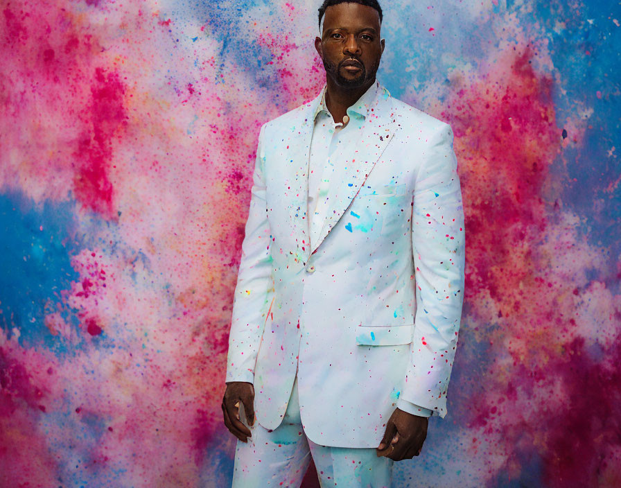 Man in White Suit with Colorful Paint Splatters Against Abstract Blue and Pink Backdrop