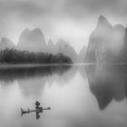 Tranquil river with boat, traditional buildings, and misty karst mountains