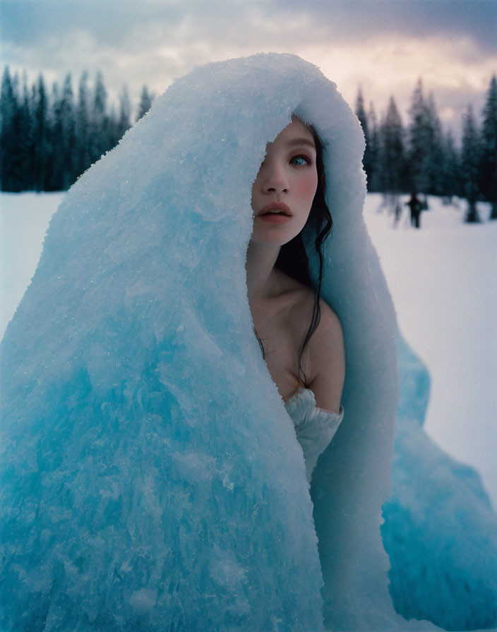 Woman covered in translucent blue ice sheet in snowy landscape.