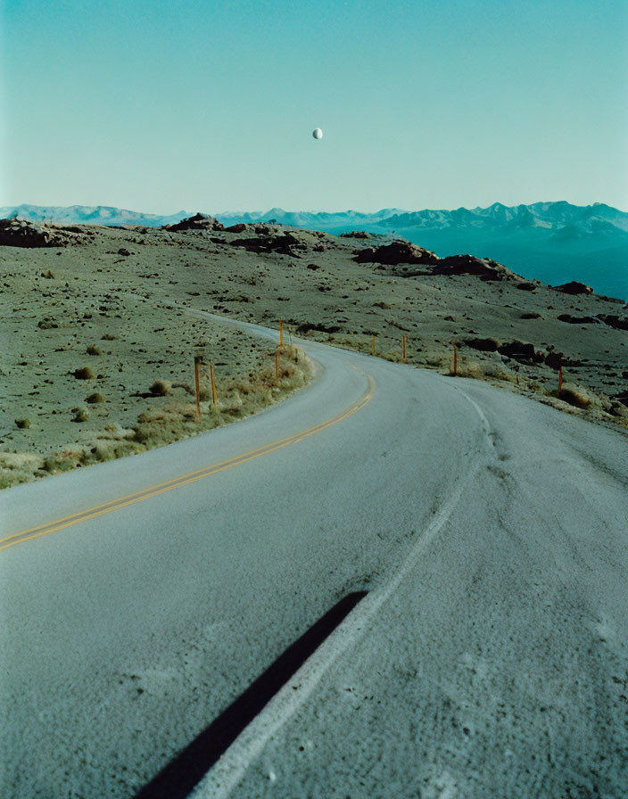 Barren landscape with winding road under clear sky and visible moon