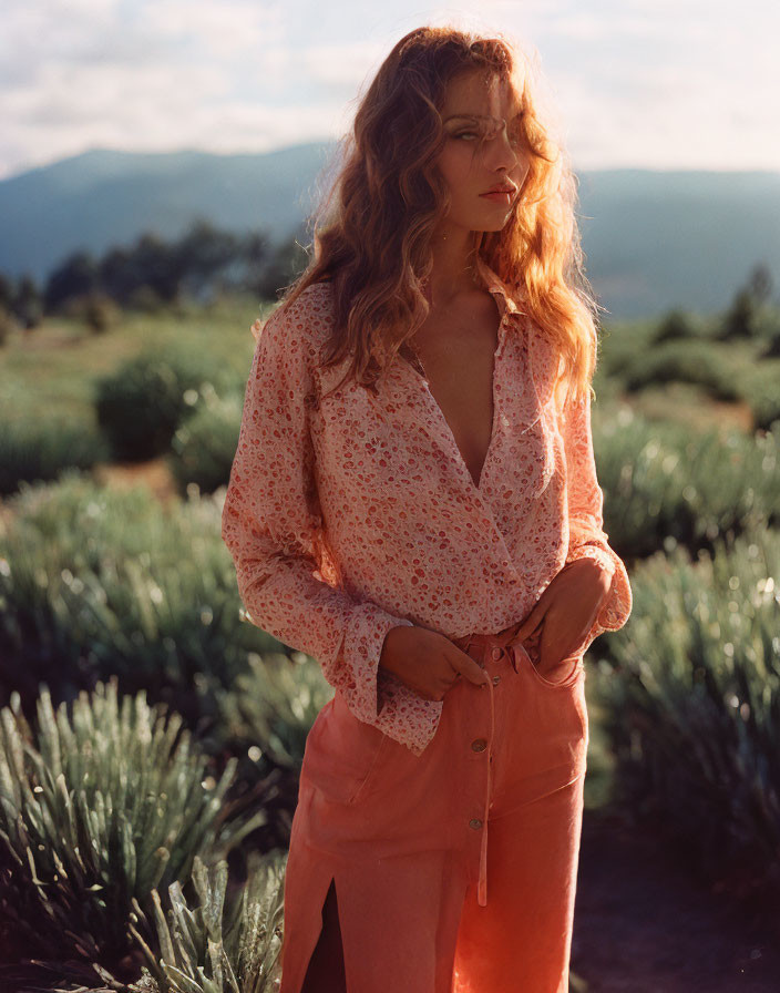 Woman in floral blouse and coral pants surrounded by agave plants and mountains under warm sunlight