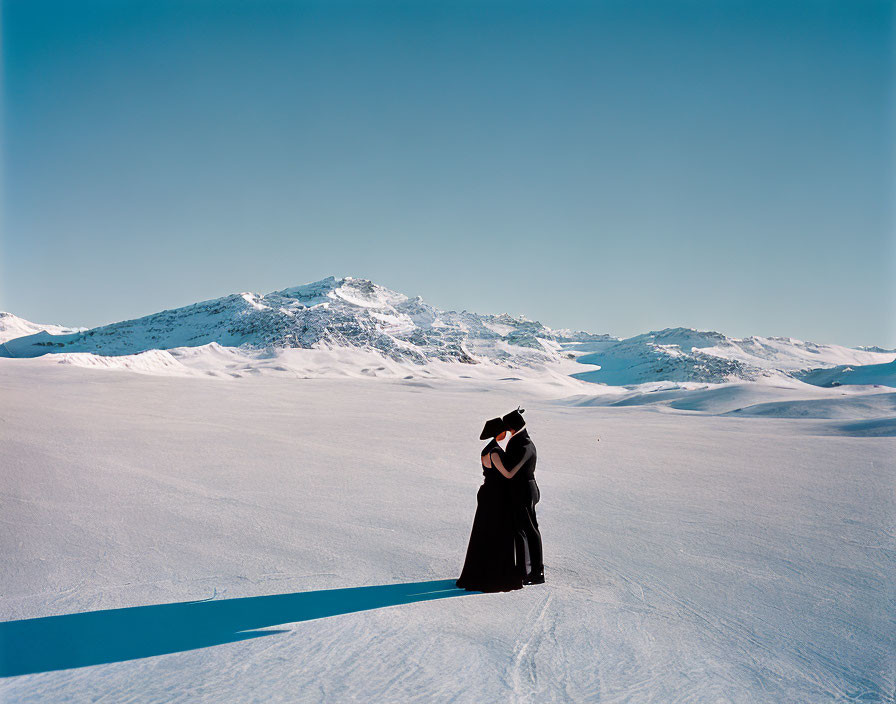 Embracing couple on snowy landscape with mountain range and blue sky