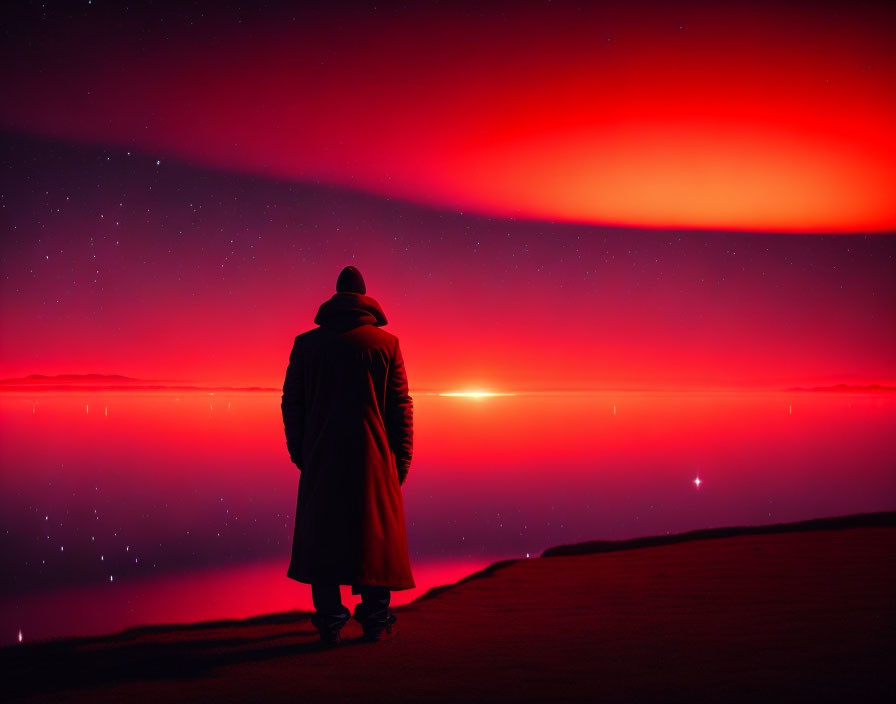 Person in coat gazes at red night sky on shoreline