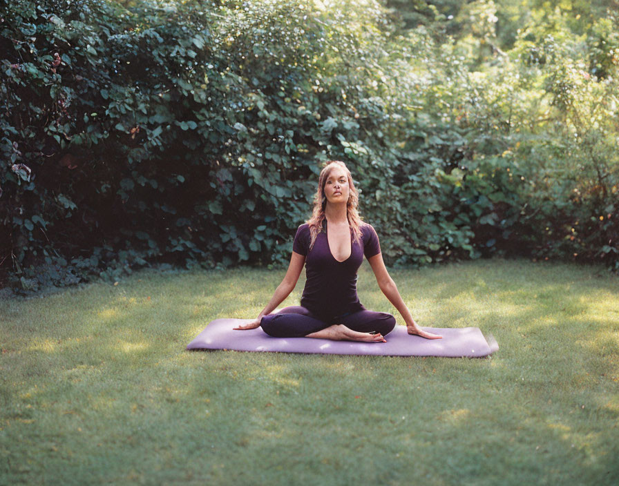 Person meditating on purple yoga mat in sunny grassy area