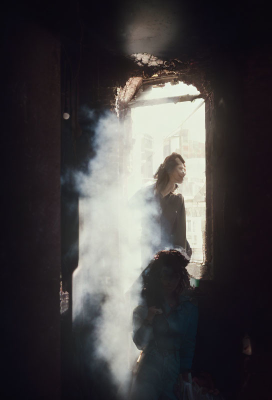 Two women in dimly lit room with light ray and dust particles.
