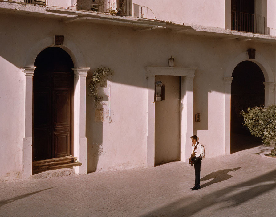 Person walking by old building with arched doorways in warm sunlight