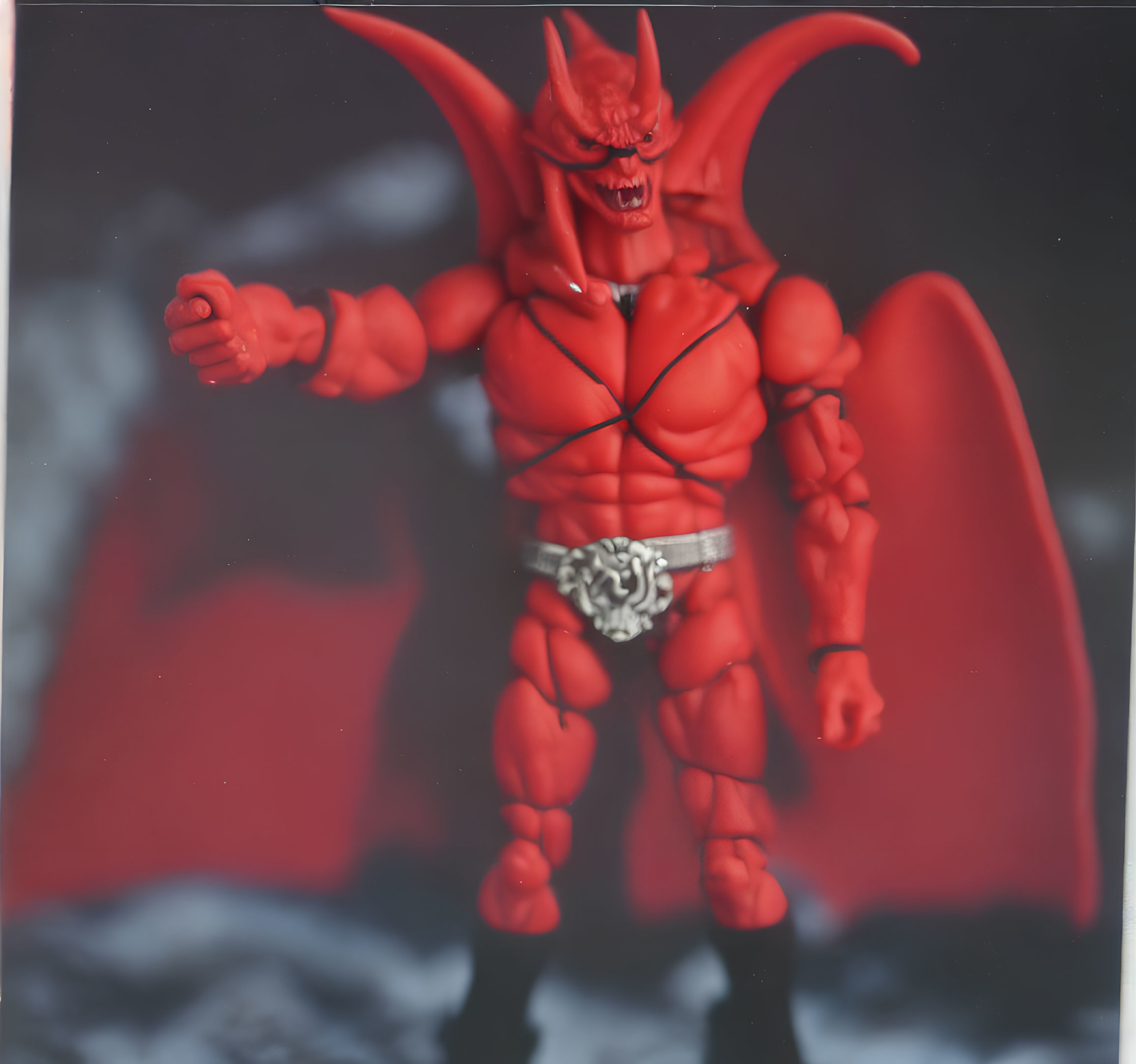 Red devil action figure with horns and wings in smoky backdrop.