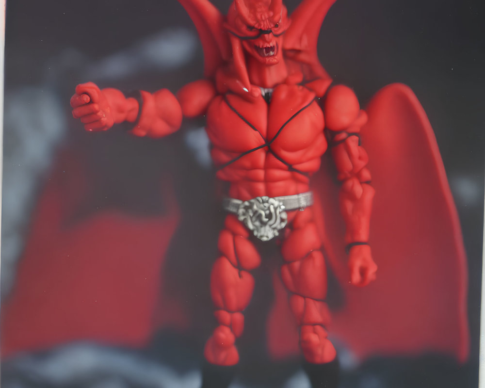 Red devil action figure with horns and wings in smoky backdrop.