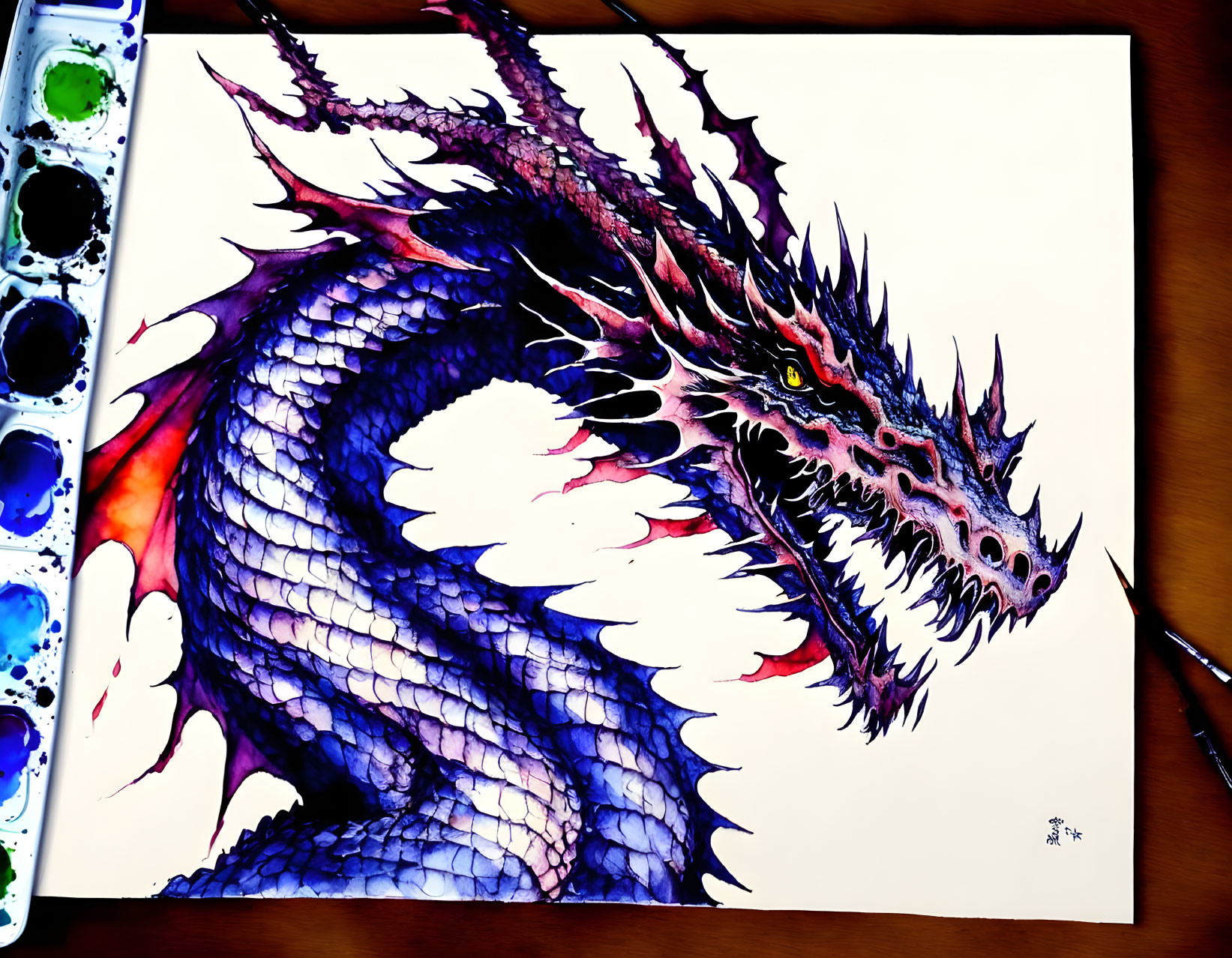 Colorful hand-painted dragon with detailed scales next to watercolor palette and brush
