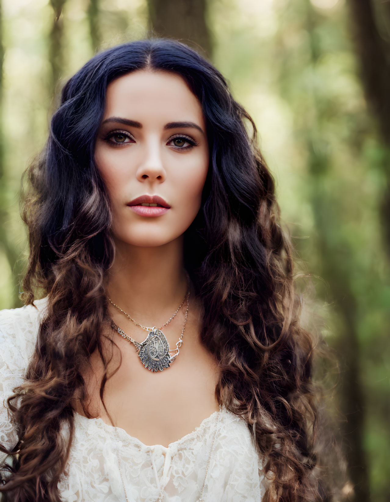 Woman with long wavy hair in lace top and pendant necklace against forest backdrop