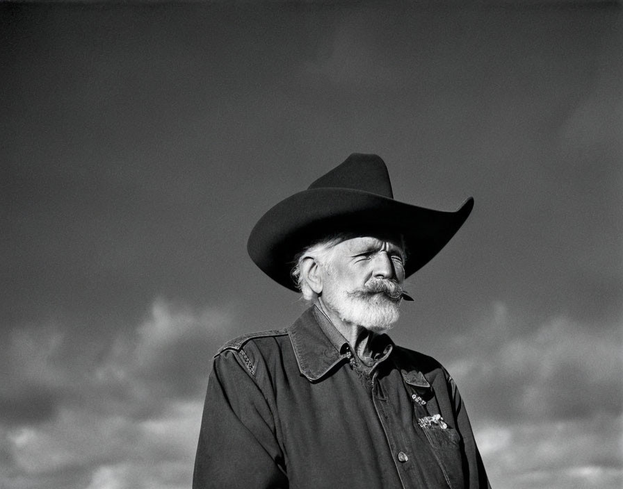 Elderly man in cowboy hat with mustache and straw, cloudy sky backdrop