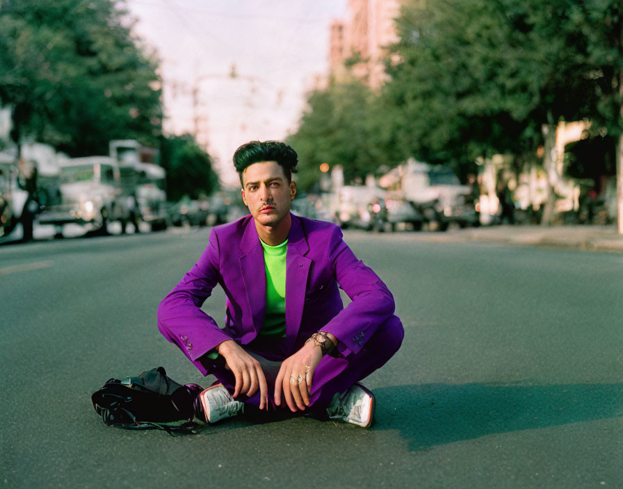 Man in Purple Suit Sitting Cross-Legged on City Street with Trees and Cars