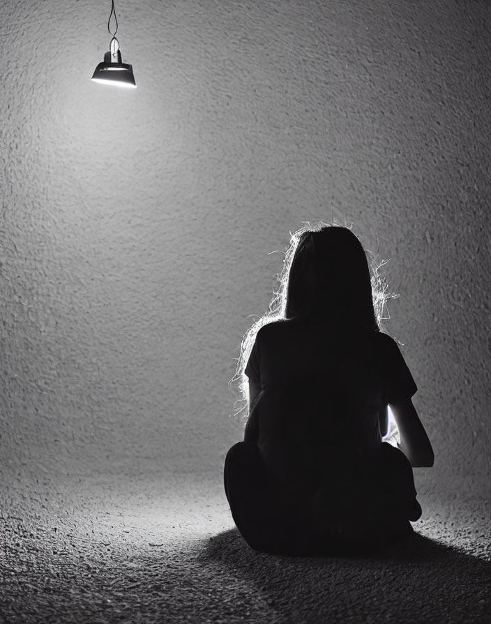 Silhouetted person seated under hanging light in dark room