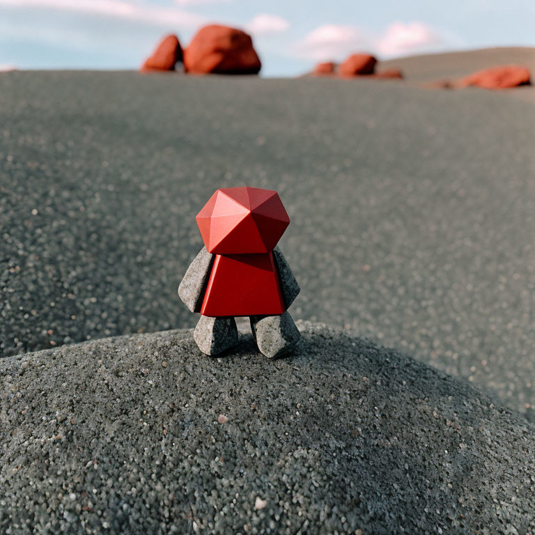 Geometric red and gray figurine on sandy surface with red rocks and blue sky
