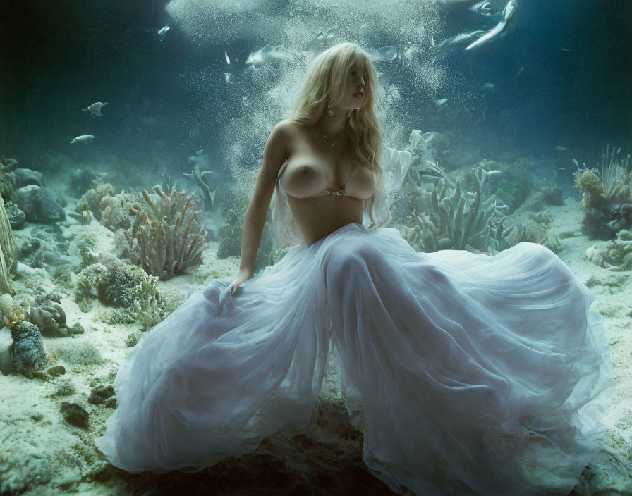 Woman in flowing dress underwater surrounded by fish and coral, hair floating.