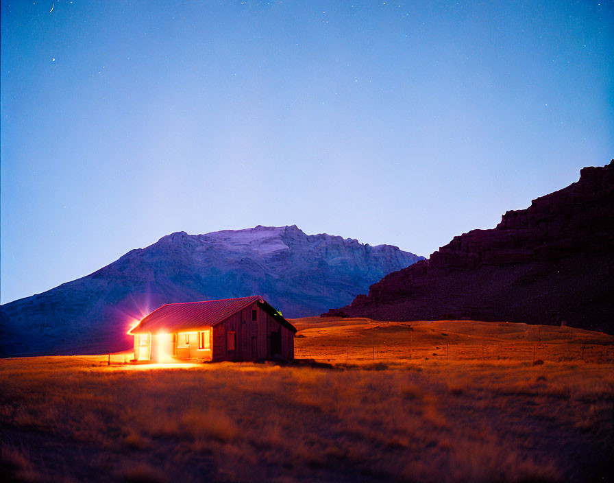 Isolated house under starry sky with looming mountain at dusk.