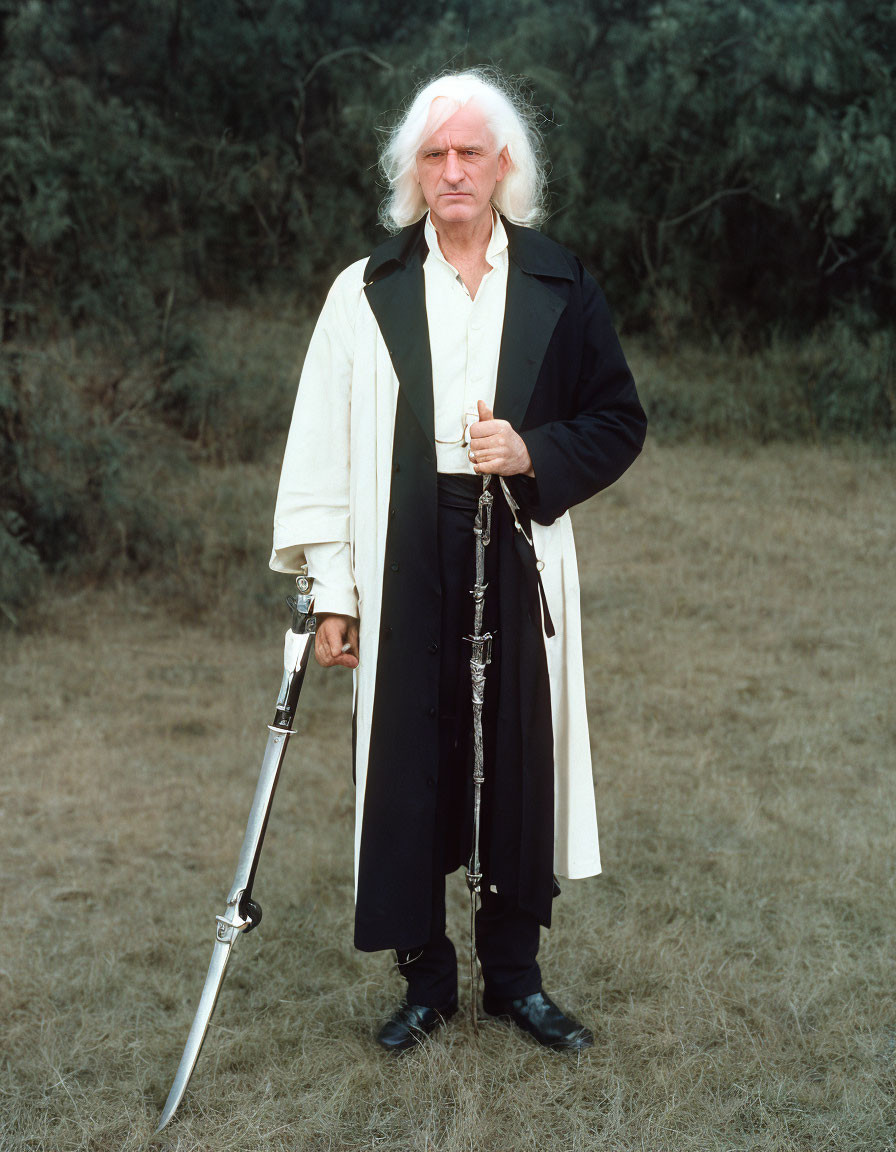 Elderly man with white hair and beard in field holding staff with sword blade wearing robe