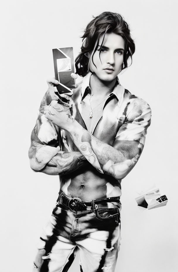 Long-haired person with tattoos holding a card in open shirt and jeans on white background