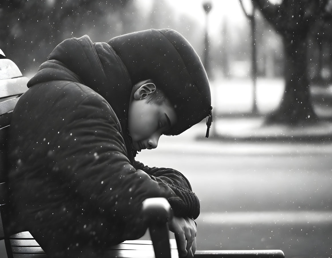 Person sleeping on park bench as snowflakes fall