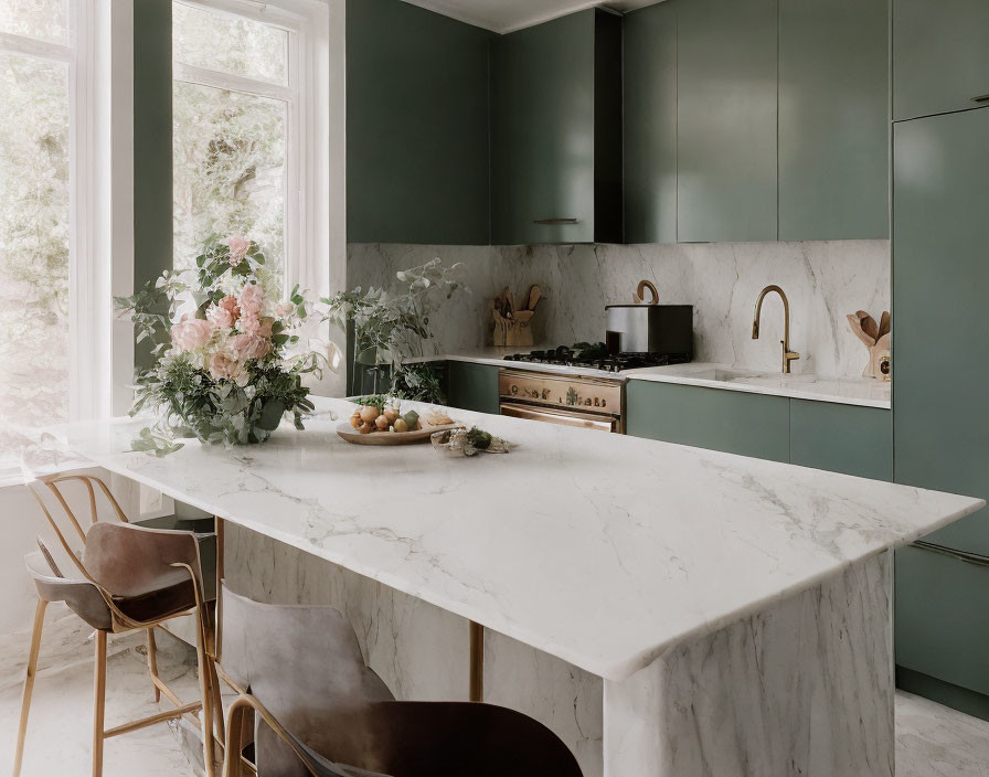 Modern kitchen with dark green cabinets, marble countertops, central island, brass fixtures, and natural light.