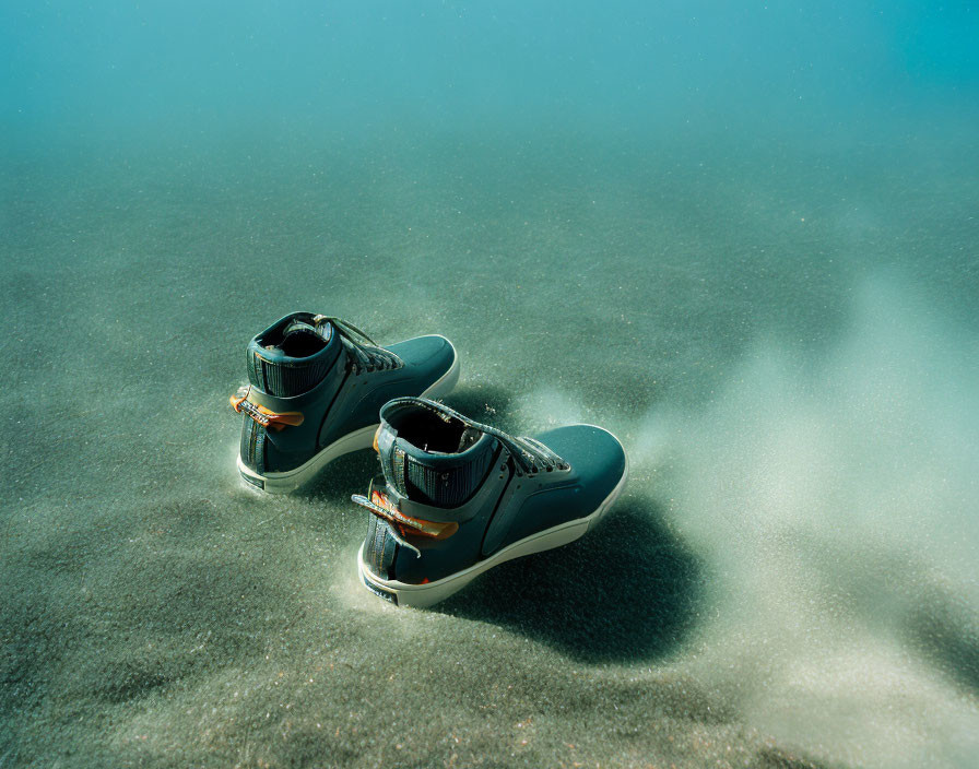 Black hiking boots with orange laces submerged in clear water on sandy ground