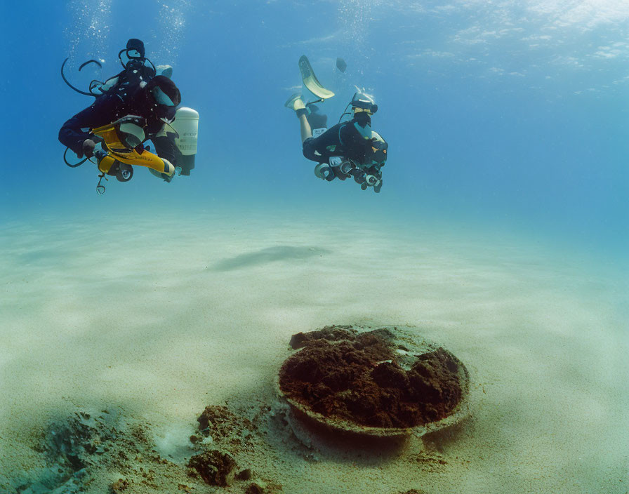 Underwater scuba divers near sandy sea floor and rock formation