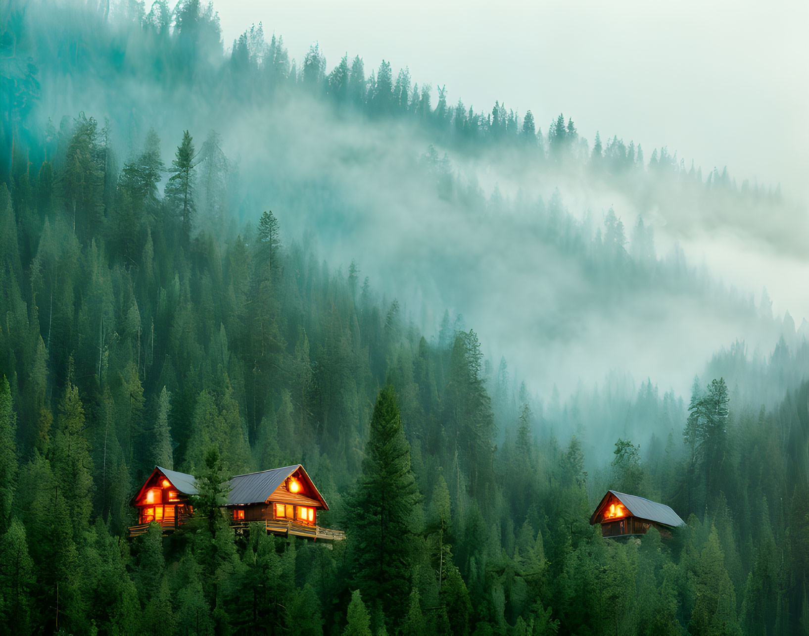 Illuminated cabins in misty forested mountain landscape