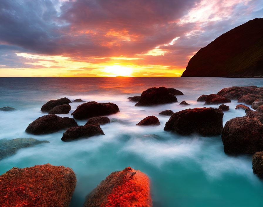 Colorful sunset over calm ocean with dramatic sky and mossy rocks contrasting fiery horizon