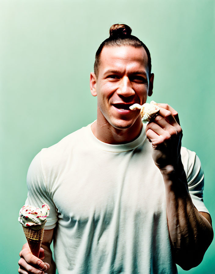 Man with topknot hairstyle smiling with ice cream cone on teal background