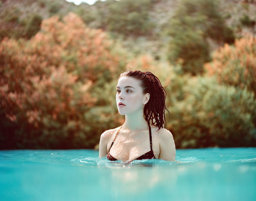 Woman with wet hair in serene water, surrounded by autumn trees