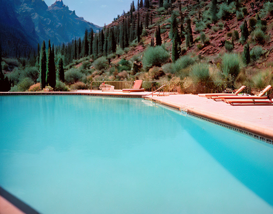 Tranquil outdoor swimming pool with blue water, sun loungers, greenery, and mountains.