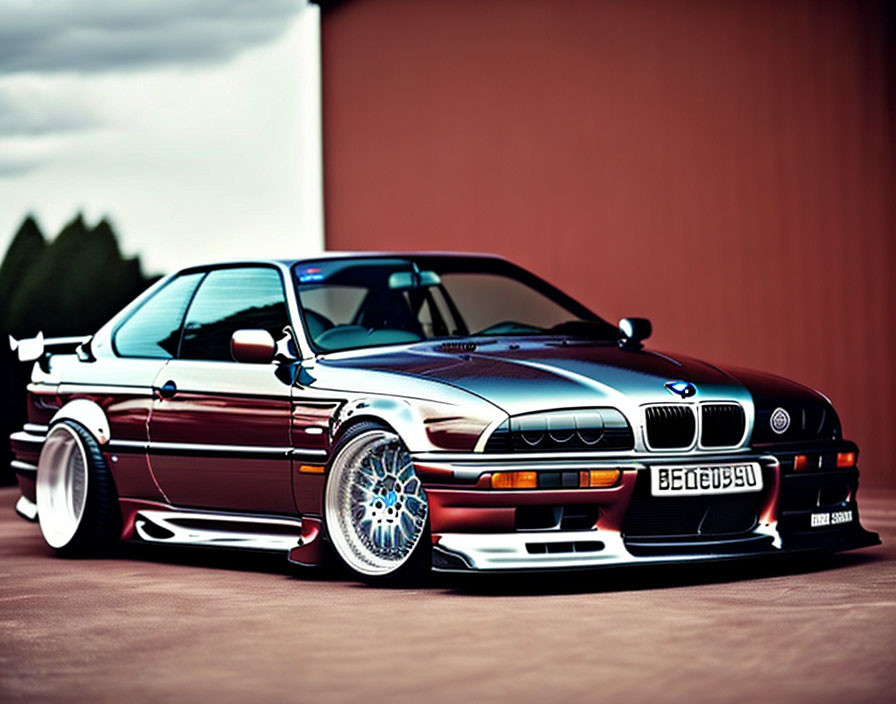 Customized BMW E36 with front splitter, aftermarket wheels, and rear wing against reddish-brown