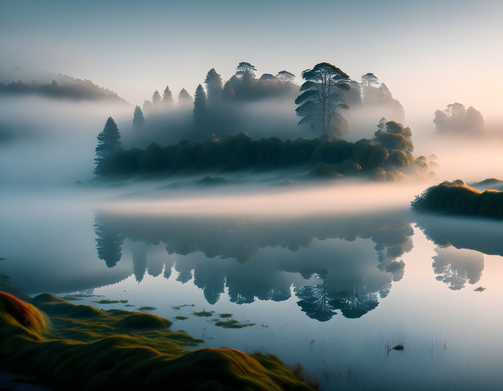 Tranquil foggy lake scene with trees reflected in mist