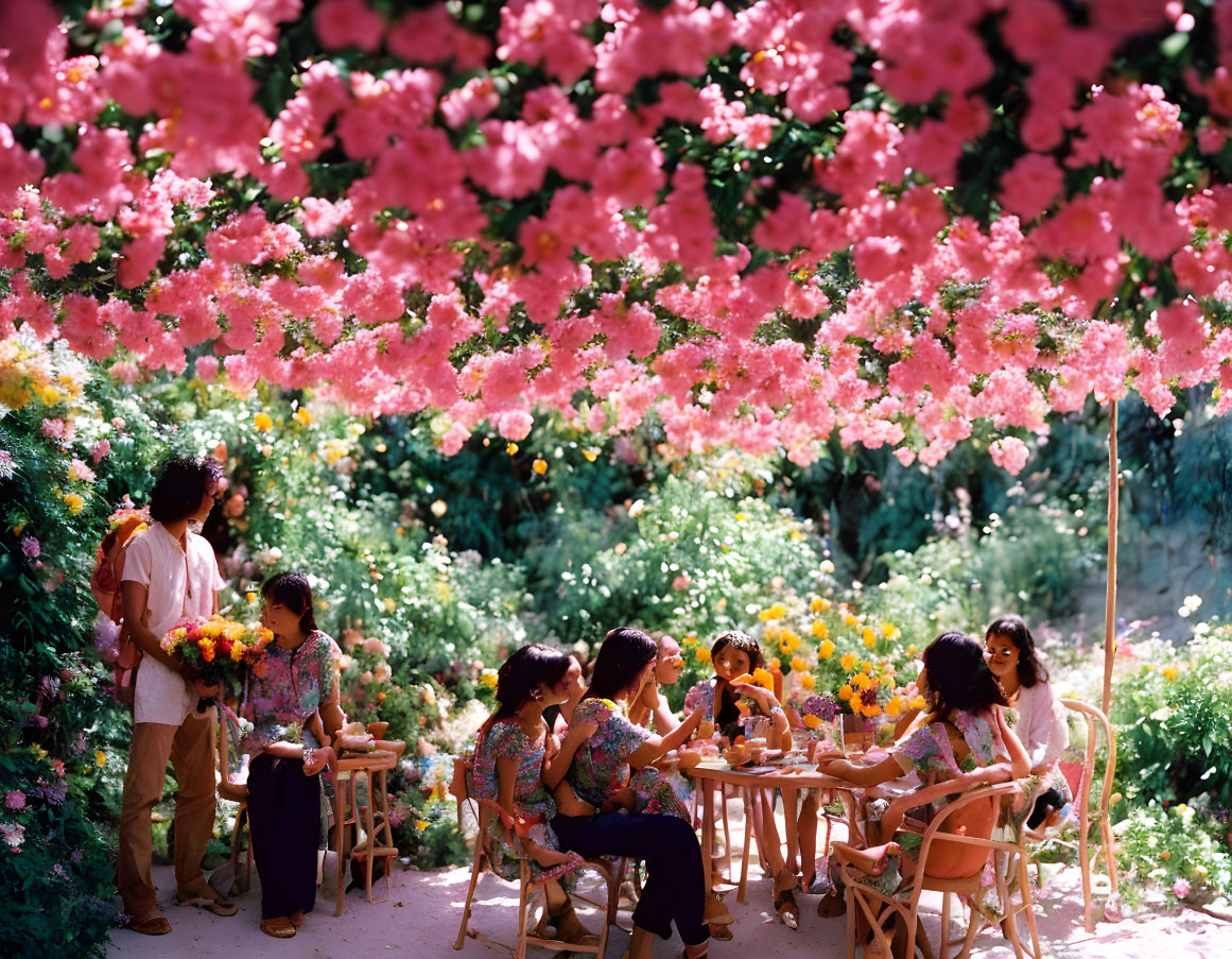 Group dining under vibrant pink blossoms in lush garden setting