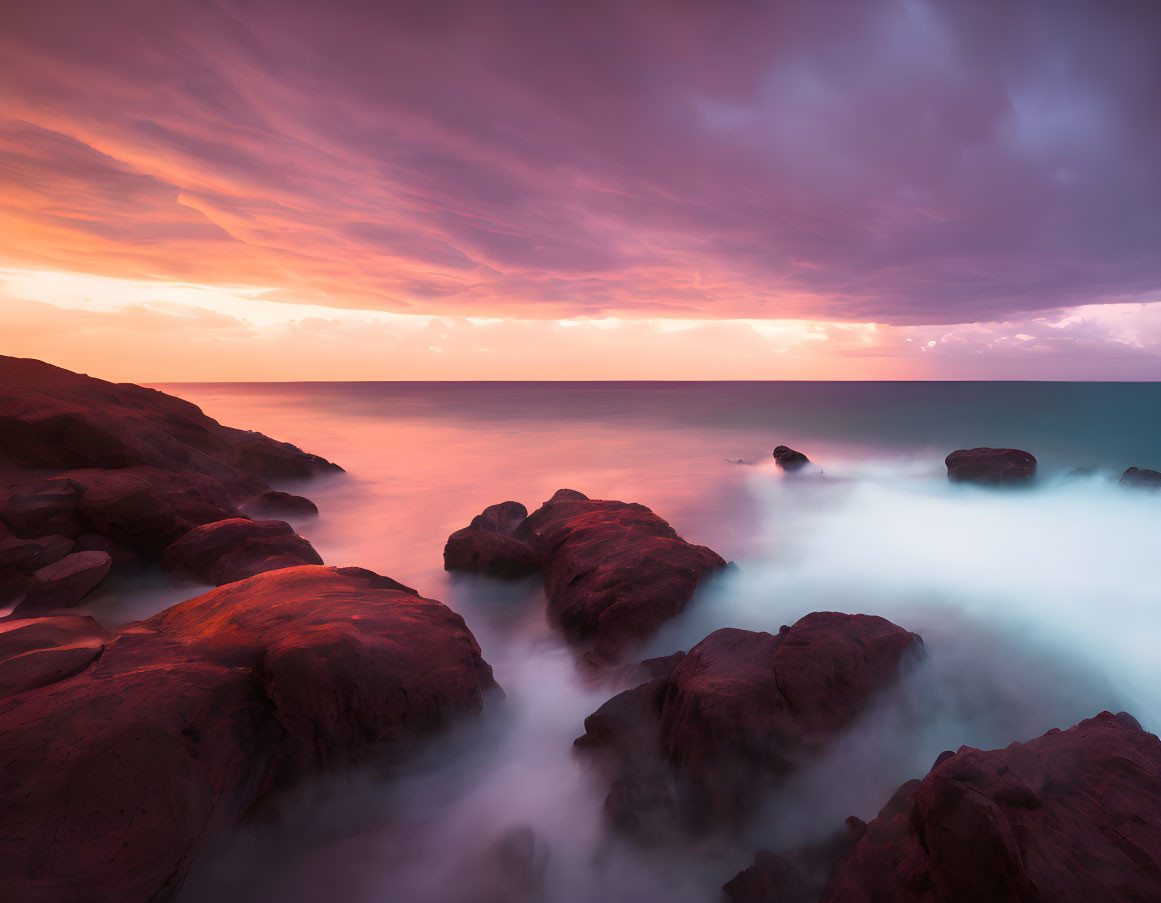 Twilight Seascape: Smooth Water, Red Rocks, Vibrant Purple and Orange Sky