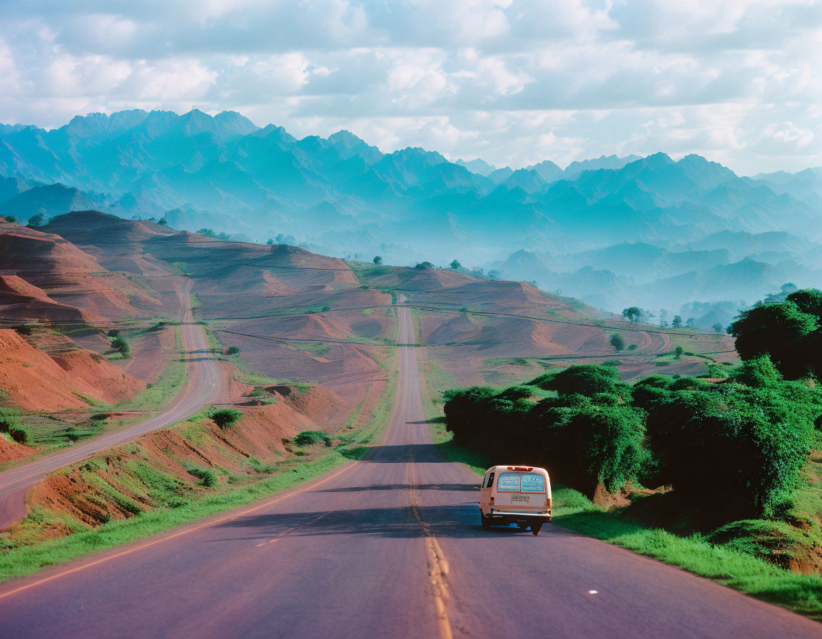 Van driving on straight road through hilly landscape with blue mountains and cloudy sky