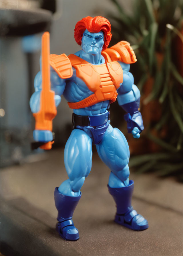 Exaggerated muscle red-haired action figure in blue and orange costume with orange gun against plant backdrop